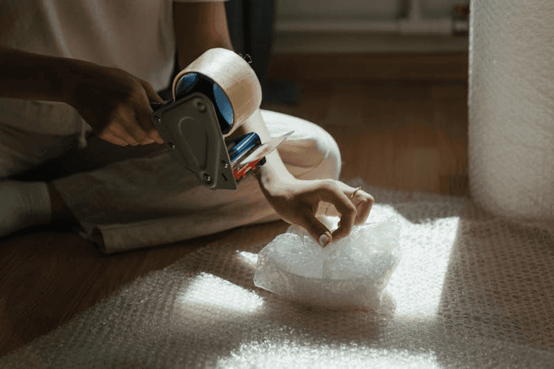 A person uses bubble wrap and tape to pack an item.png
